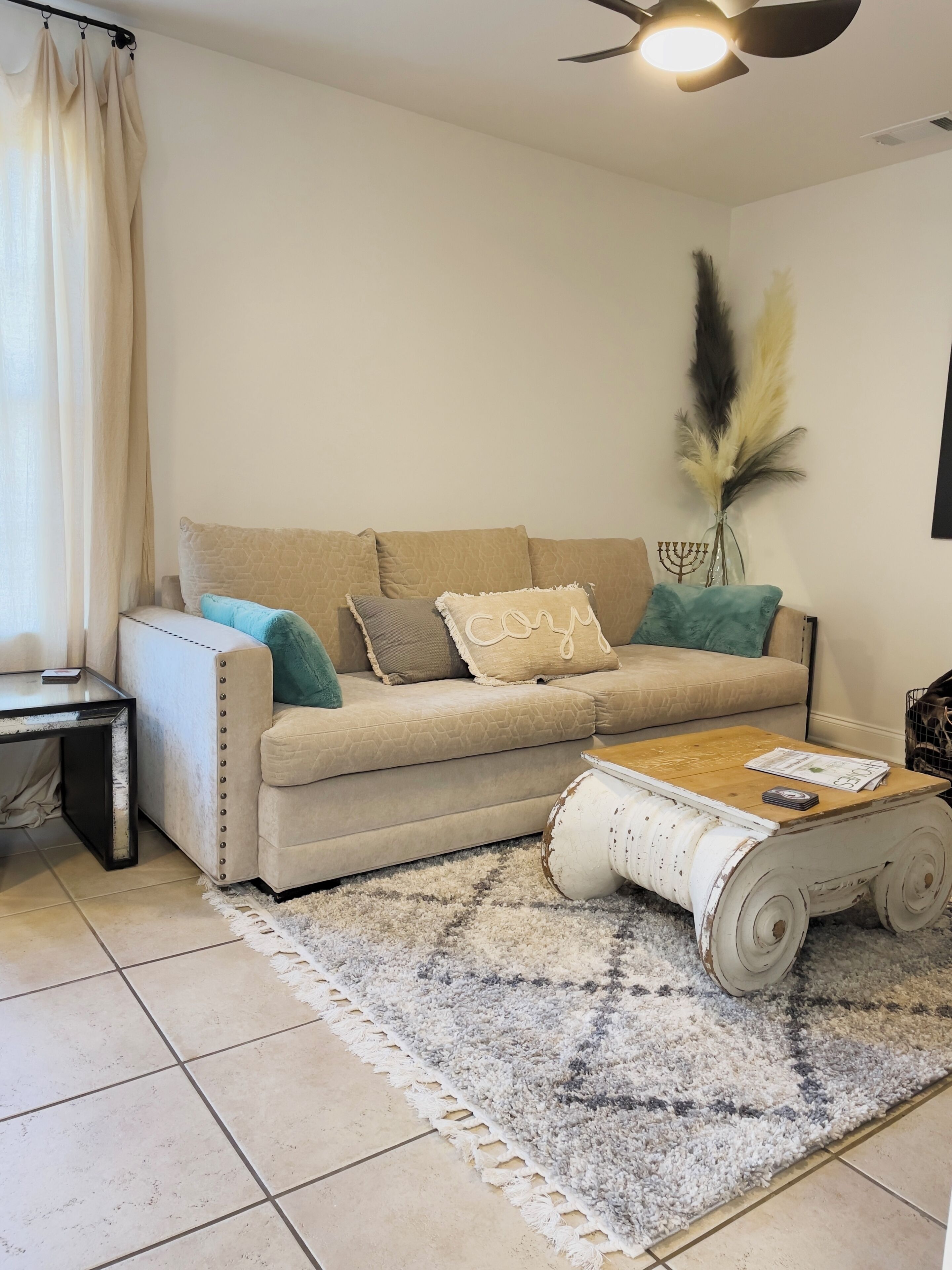 A living room with a beige sofa, a coffee table, a rug, a wall-mounted menorah, and a ceiling fan.