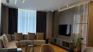 Uma sala de estar moderna com sofá seccional, mesa de jantar de mármore e televisão de tela plana fixada em uma parede de painéis de madeira.