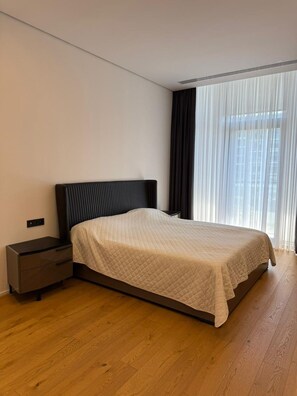 Un dormitorio moderno con una cama, una mesita de noche y una ventana con cortinas translúcidas.