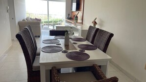 Een eetgedeelte met een witte tafel, geweven stoelen en ronde placemats.