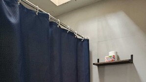 Ein Badezimmer mit Toilette, einer dunkelblauen Duschvorhangs und einem Ablagebereich mit Toilettenpapier und einer Flasche.