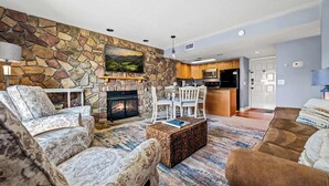 A living room with a stone wall, fireplace, and a dining area with chairs and a table. - Mountain View Condo w/ Indoor Pool & Golf Access (Gatlinburg)