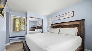 A bedroom with a large bed, a window with blinds, a mirror, and a sign on the wall. - Mountain View Condo w/ Indoor Pool & Golf Access (Gatlinburg)