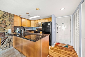 A modern kitchen with granite countertops, wooden cabinets, a stone accent wall, a black refrigerator, and a microwave. - Indoor Pool, Balcony & Fireplace , Mountain Views (Gatlinburg)