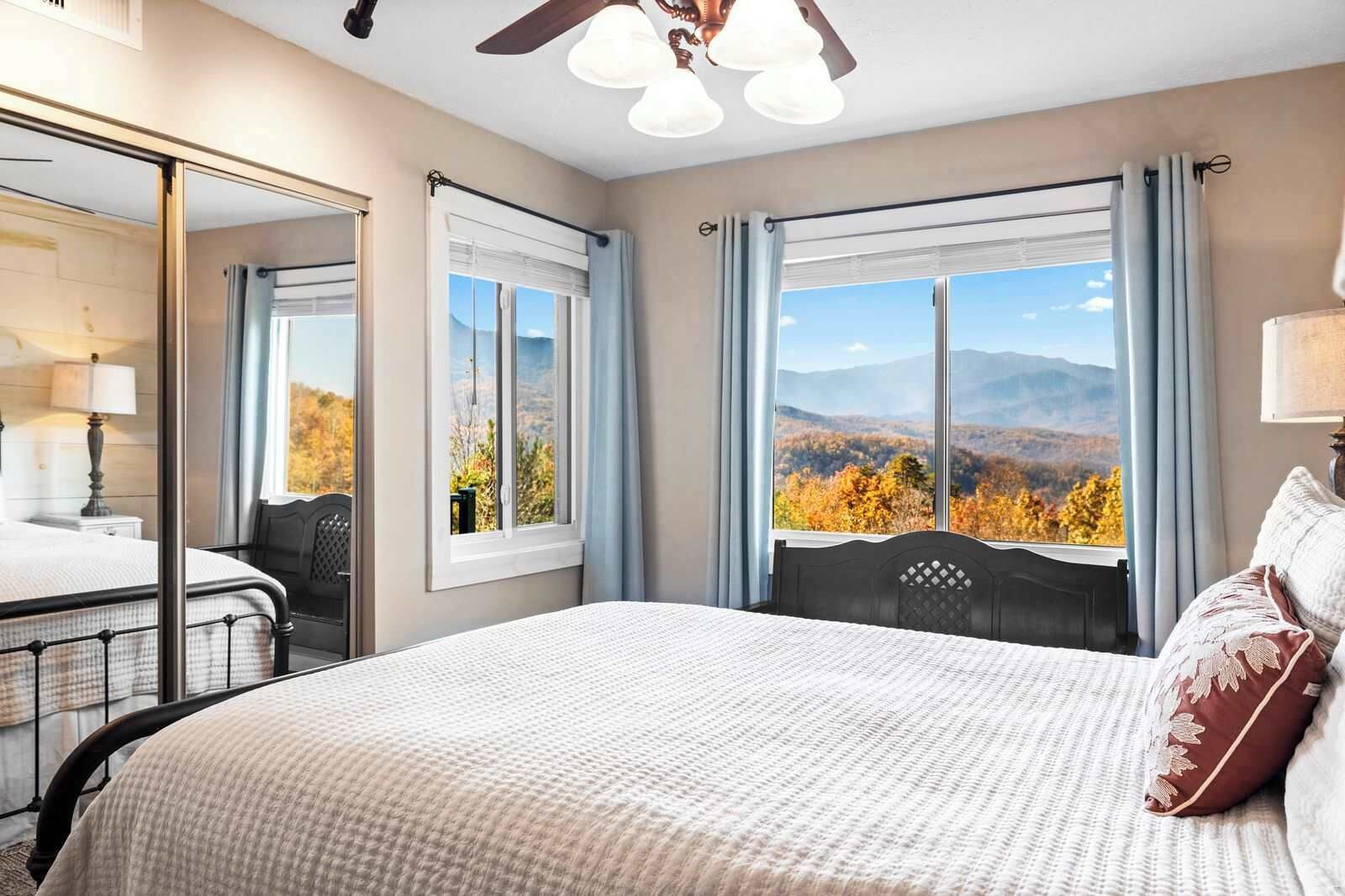 Ein Hotelzimmer mit Bett, Schreibtisch, Stuhl, Spiegel und Blick auf Herbstlaub.