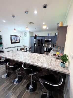 Una cocina moderna con encimeras de granito, electrodomésticos de acero inoxidable y taburetes de bar.