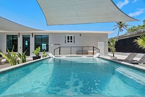 A swimming pool with lounge chairs and a shaded area, surrounded by a building with large windows and a door.