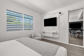 A modern hotel room with a bed, a TV, a chair, and a dining area visible through a glass door. - Balandras Beach Stay 1 Beach & Pool Access (Dorado)