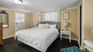 Een slaapkamer met een bed, nachtkastjes, een spiegel, een deur en een raam met gordijnen.