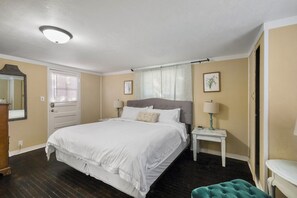 A bedroom with a bed, bedside tables, a mirror, a door, and a window with curtains.