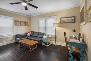 A living room with a sofa, coffee table, lamp, and a desk with chair.