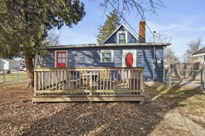A blue house with a red door, a wooden deck, and a chimney.