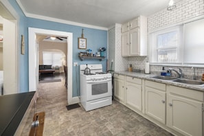 A kitchen with white cabinets, a stove, a sink, and a window with blinds.