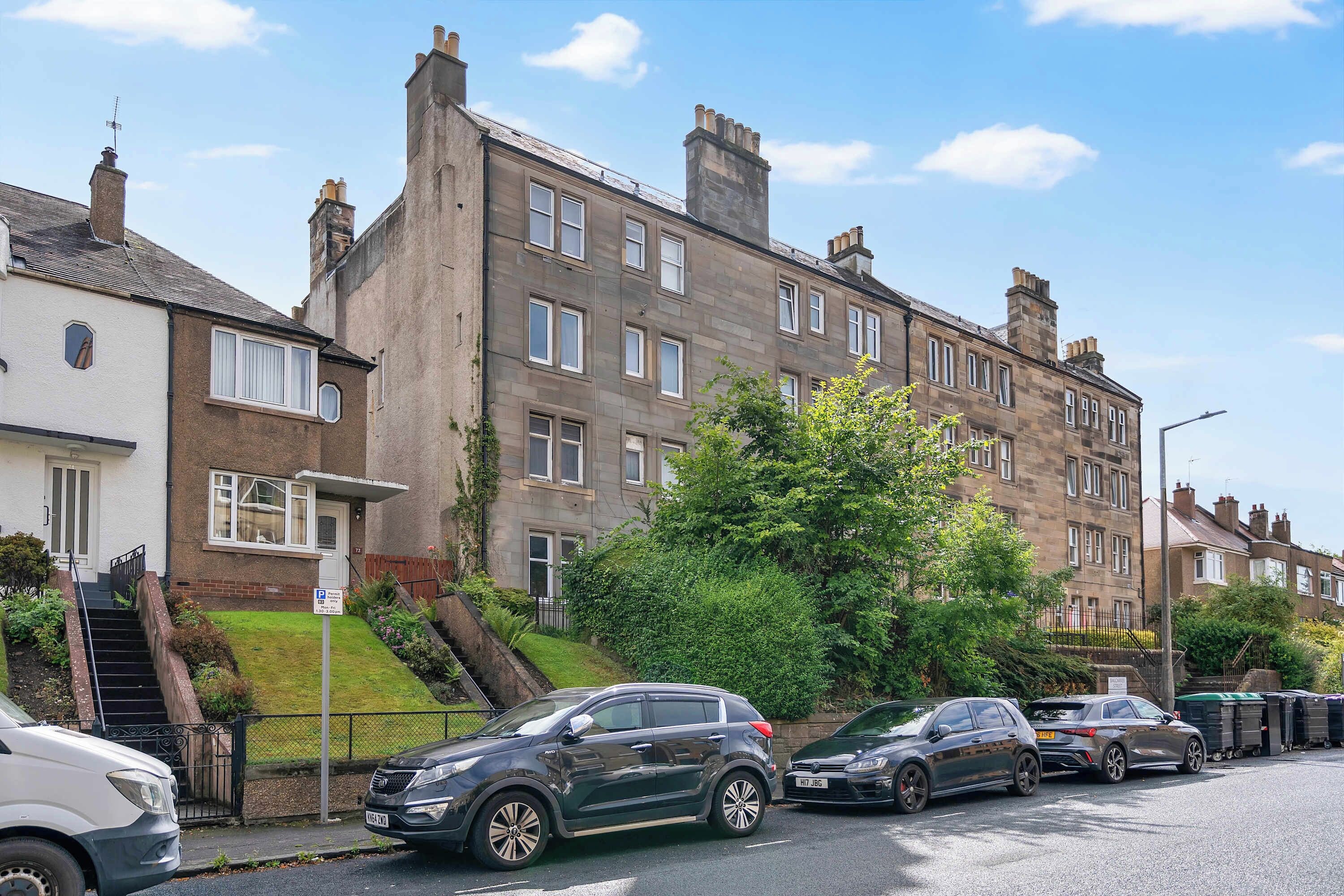 A residential street with terraced houses, parked cars, and a clear sky.