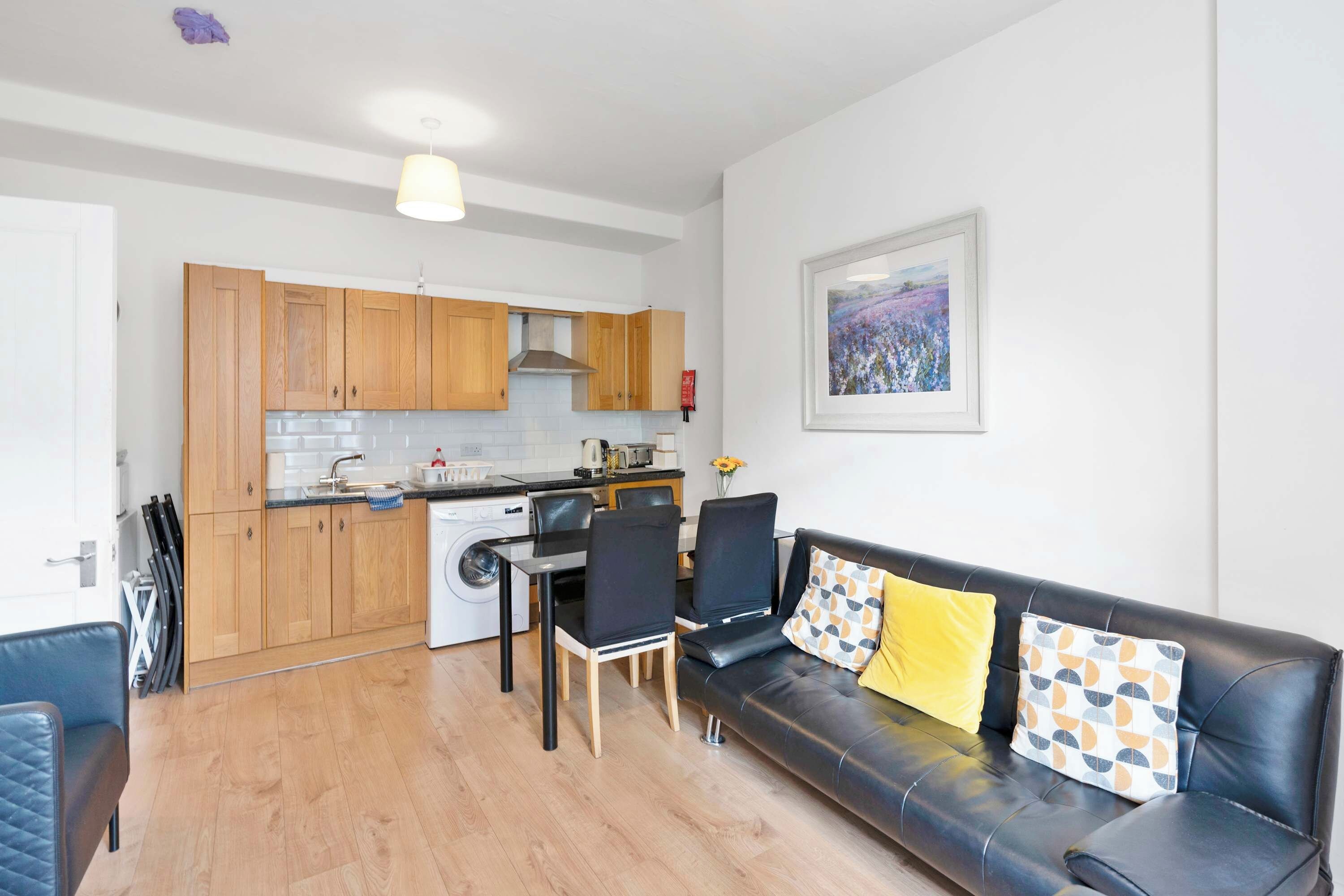 A modern kitchen with wooden cabinets, a built-in oven, and a dining area with a black leather sofa and chairs.