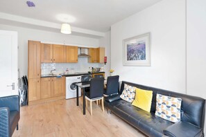 A modern kitchen with wooden cabinets, a built-in oven, and a dining area with a black leather sofa and chairs. - Morningside 2BR, Direct Bus to Old Town Edinburgh (Edinburgh)