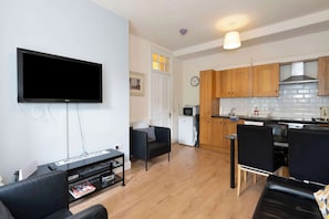 A modern living room with a flat-screen TV, a sofa, a coffee table, and a small side table with magazines. - Morningside 2BR, Direct Bus to Old Town Edinburgh (Edinburgh)