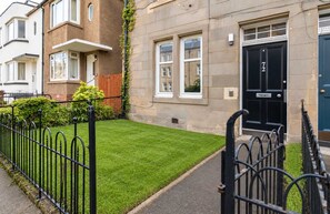 A residential building with a well-maintained lawn, a black front door, and a brick facade. - Morningside 2BR, Direct Bus to Old Town Edinburgh (Edinburgh)