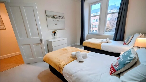 Habitación de hotel con dos camas, una mesita de noche, un ventanal con cortinas y un cuadro colgado en la pared.
