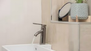Un baño moderno con lavamanos blanco, grifo cromado y un espejo encima.