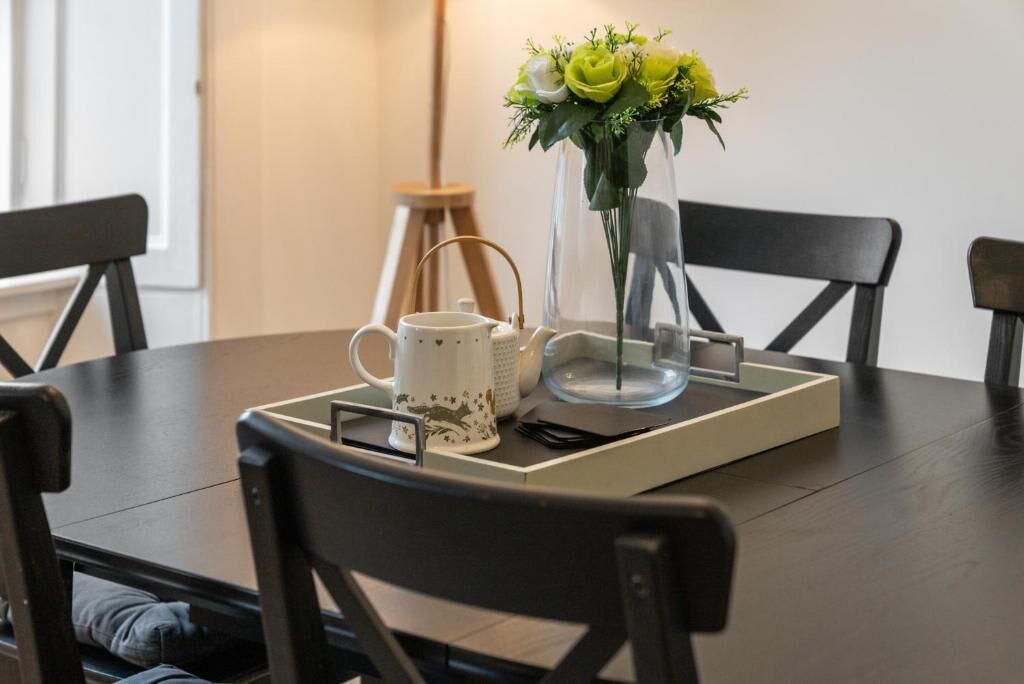 A dining table with a tray, a white mug, a teapot, and a vase with flowers.