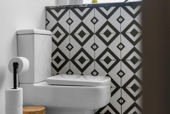 Un baño con inodoro, un rollo de papel higiénico y un papel tapiz estampado.