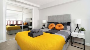Een moderne slaapkamer met een groot bed, een nachtkastje met een lamp en een spiegel.