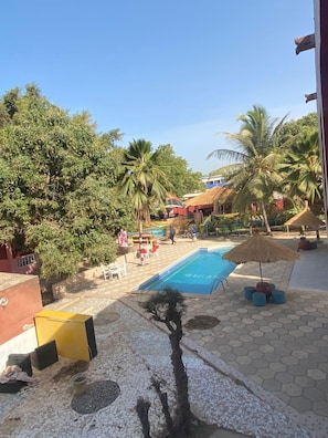 A pool area with a tiled floor, palm trees, and a thatched umbrella. - Chez carlo Oasis (Nianing)
