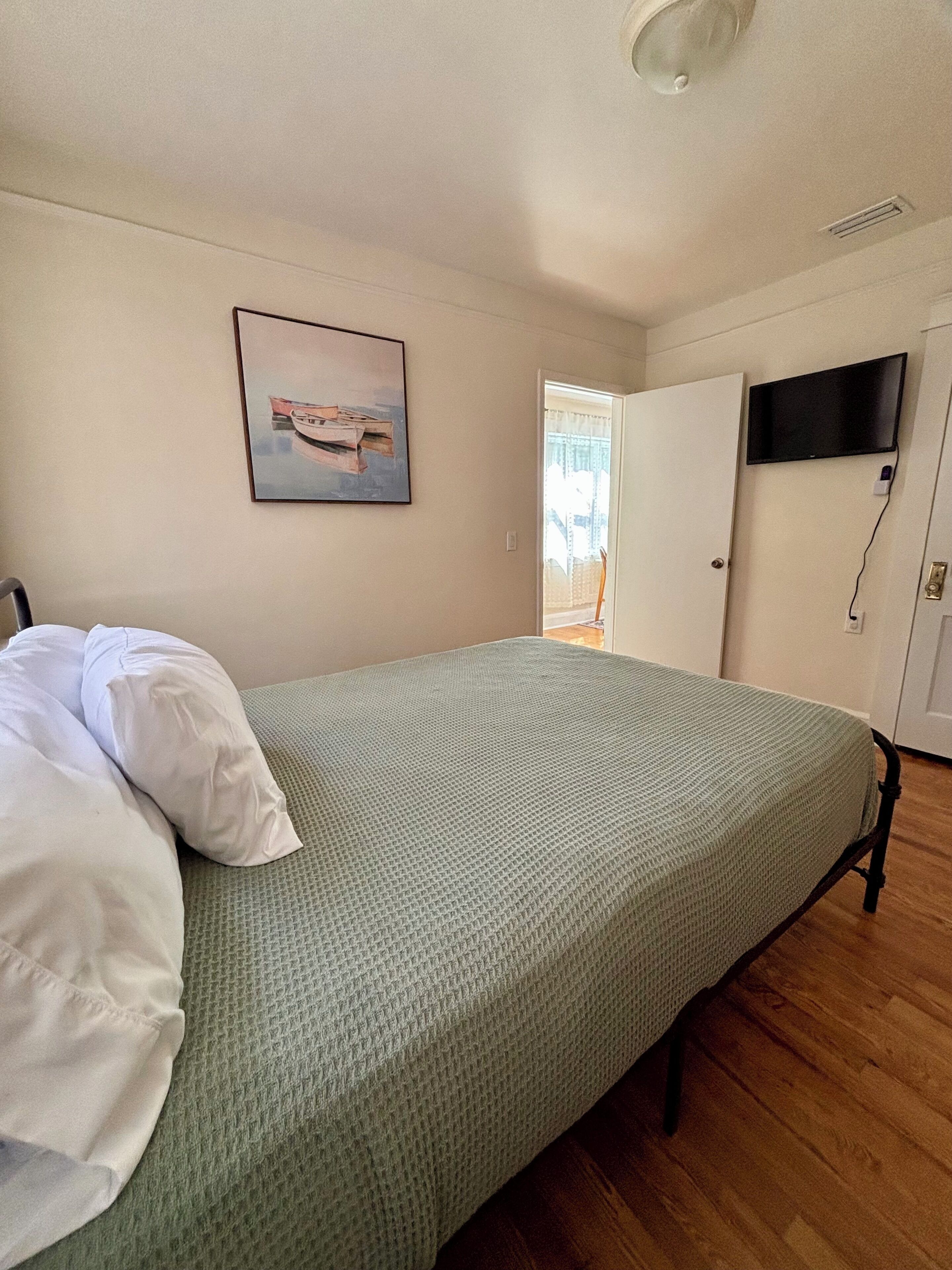 A room with a bed, a painting, a television, and a door.
