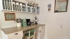 Een keuken met witte kastjes, een houten aanrecht, een koffiezetapparaat en een krantenartikel in een lijst aan de muur.