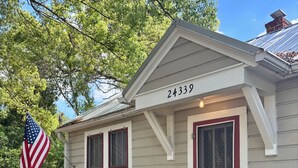 Een gelijkvloers huis met het nummer '24339' vooraan, een veranda met een witte balustrade, en een grote Amerikaanse vlag aan de linkerkant.
