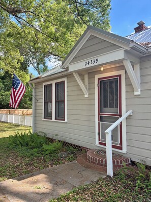 Ein eingeschossiges Haus mit der Hausnummer 24339, einem Erker mit weißer Brüstung und einer großen amerikanischen Flagge links davon.