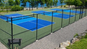 A tennis court with a net, surrounded by a fence, and a lake in the background. - Four-Season Lake Winnipesaukee Retreat (Laconia)