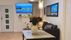 Un comedor con una mesa, bancos, lámparas colgantes, un televisor y un sofá.