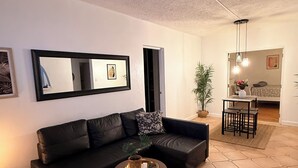 Una sala de estar con un sofá negro, una mesa redonda de centro y una zona de comedor con mesa y sillas.