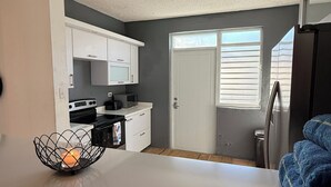 Cocina compacta con armarios blancos, microondas y cafetera. Hay una puerta que da a un balcón con vistas.