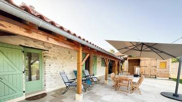 Un edificio rústico de madera con un patio de baldosas, asientos exteriores y un gran paraguas.