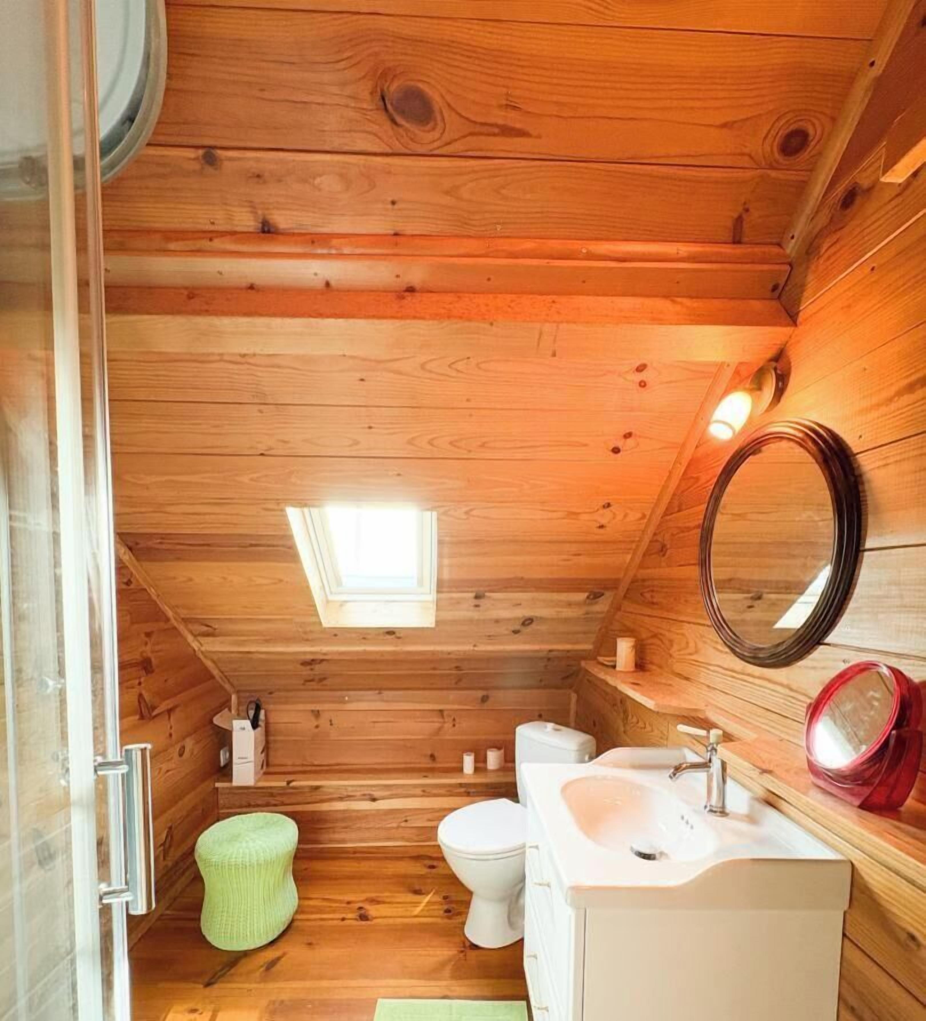 Un baño de cabaña de madera con tragaluz, un inodoro, un lavamanos y un espejo.