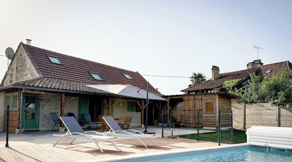 A poolside area with lounge chairs, a covered patio, and a stone building with a tiled roof. - La Mérigue - THEDIRAC - G îte (THEDIRAC)