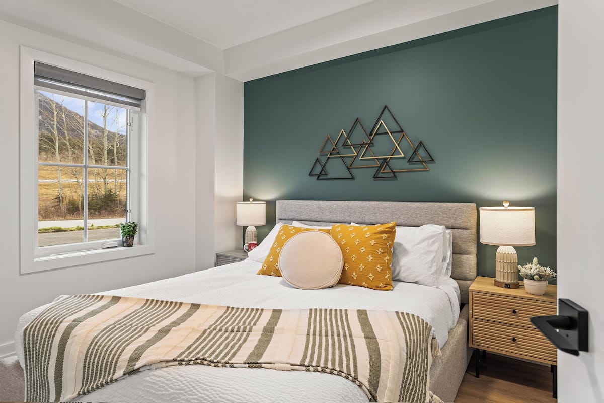 A bedroom with a bed, bedside lamps, a wall-mounted geometric decoration, and a window with a view.