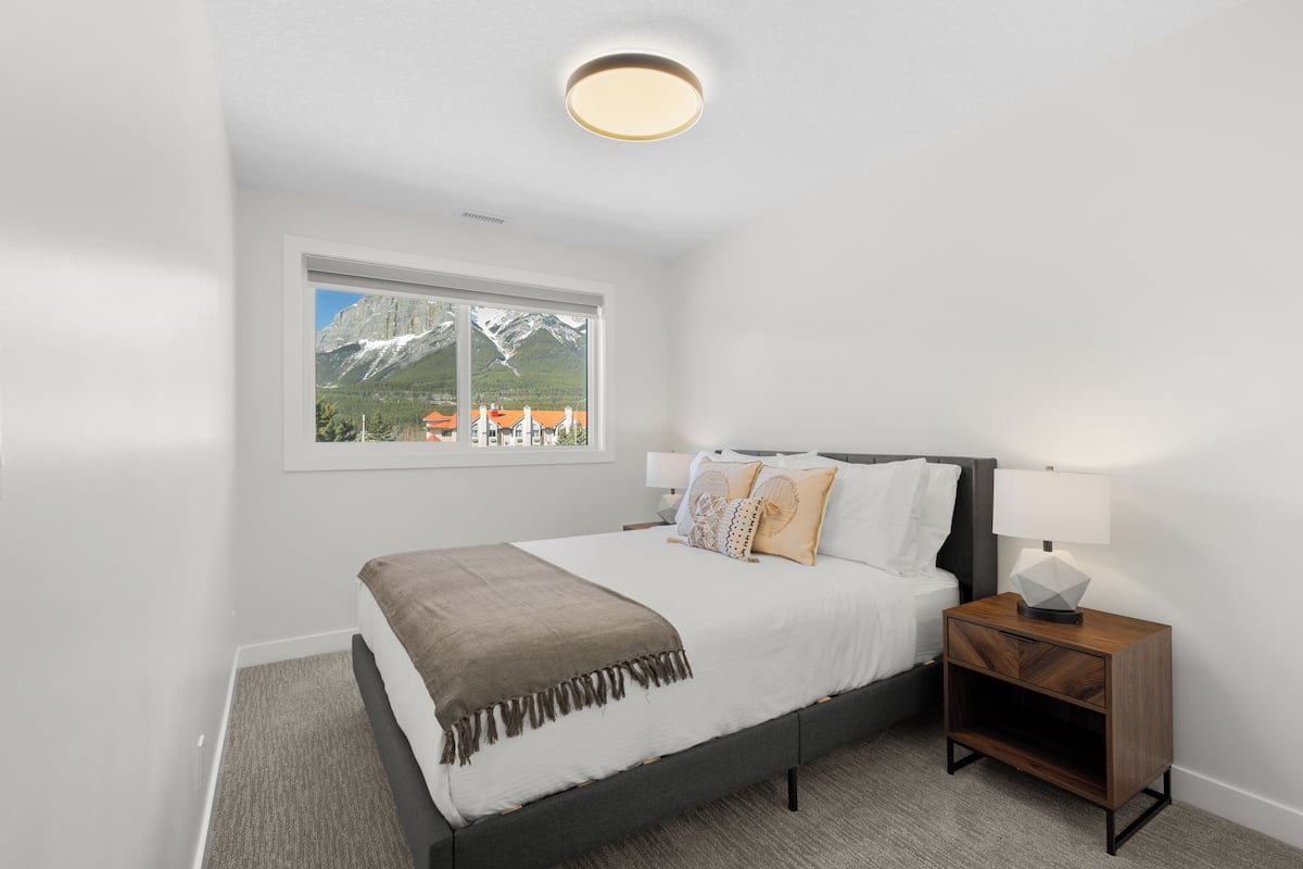 A bedroom with a bed, nightstand, lamp, and a window with a mountain view.