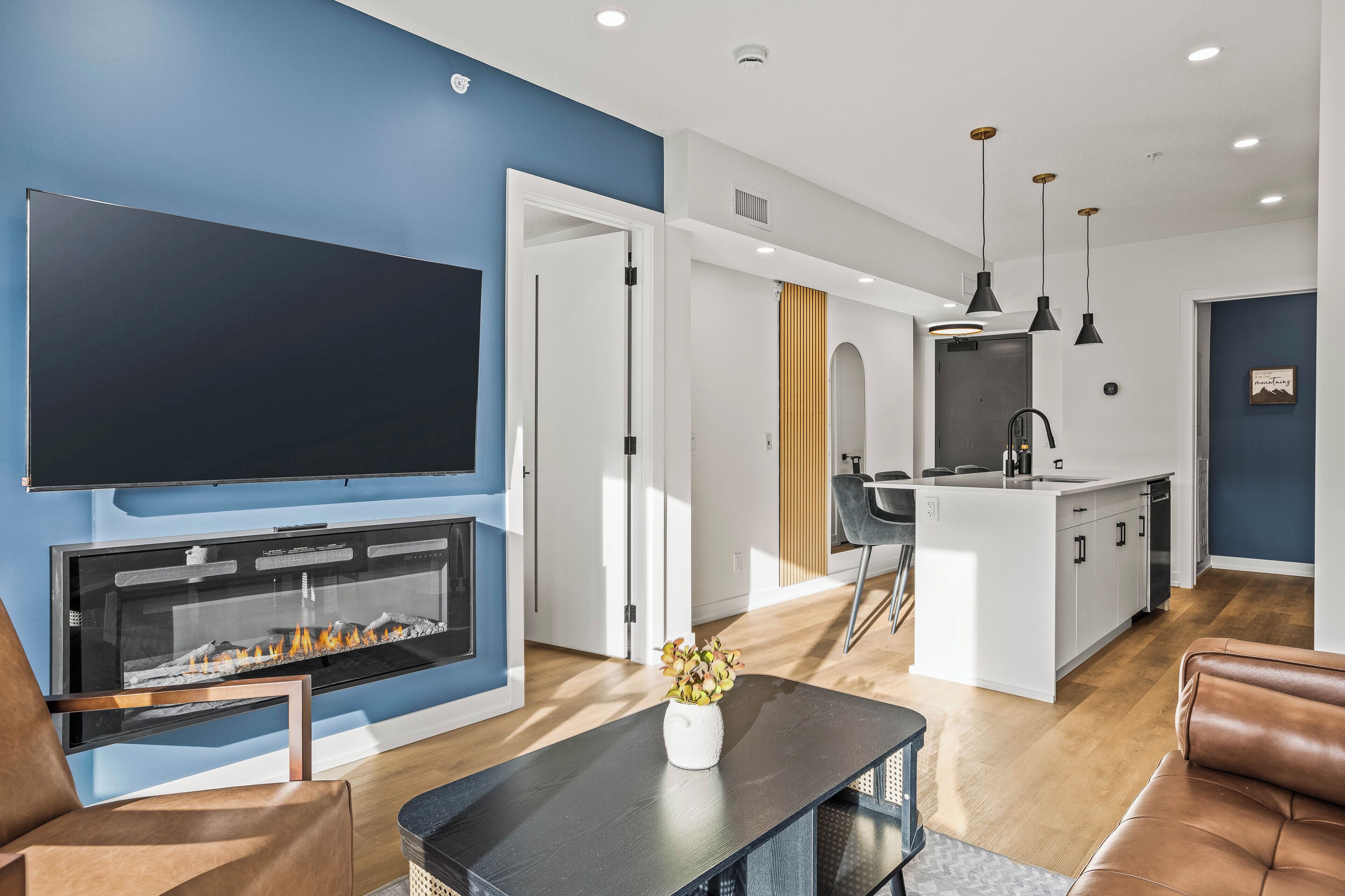 Una sala de estar moderna con chimenea, televisor de pantalla plana y comedor con cocina al fondo.