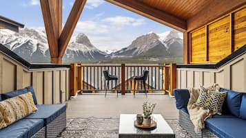 A balcony with a wooden ceiling, two blue sofas, a coffee table, and a view of snow-capped mountains.