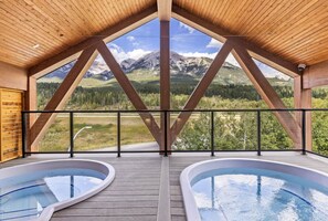 A wooden deck with two hot tubs, a wooden ceiling, and a mountain view.