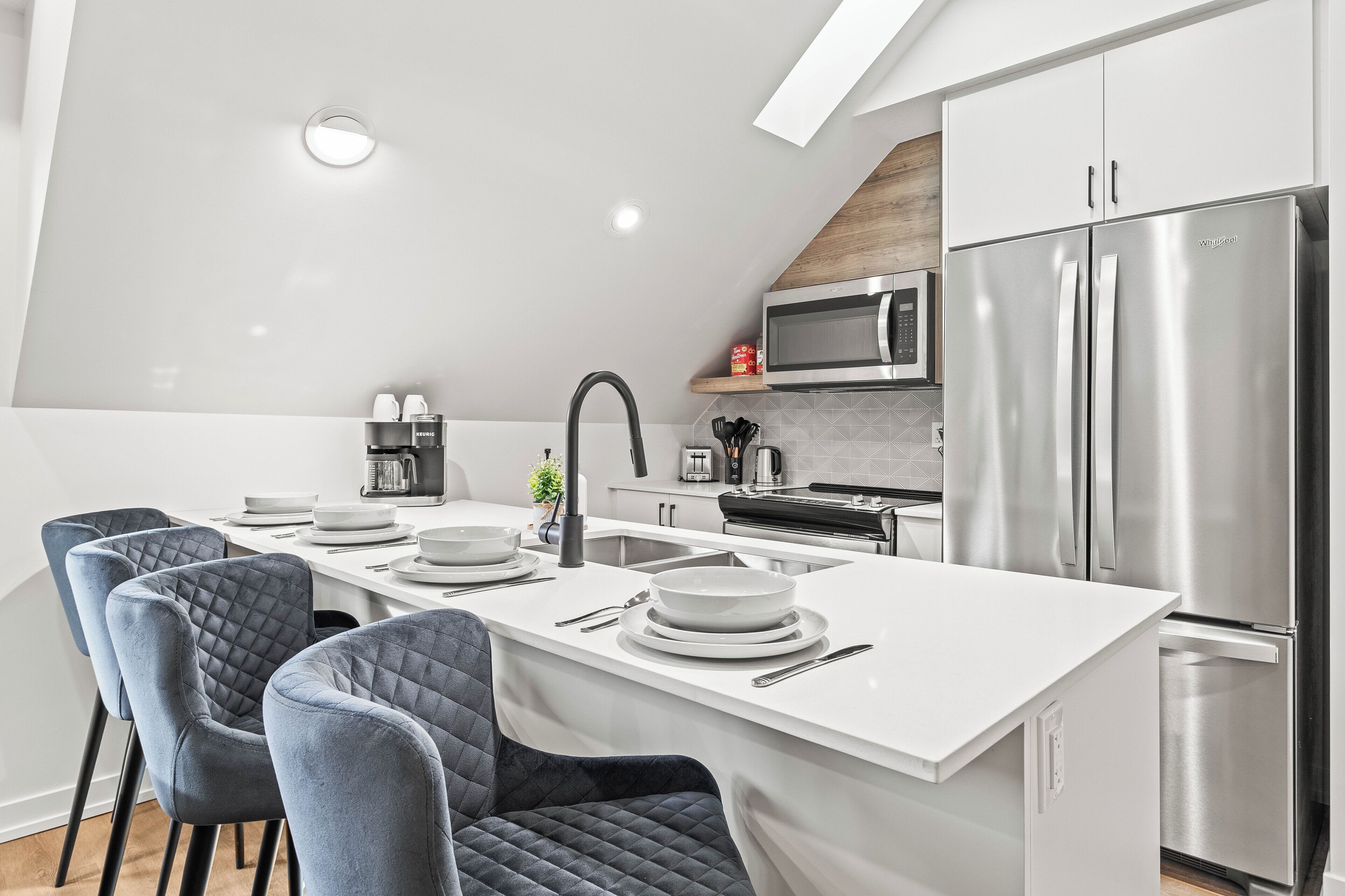 A modern kitchen with a central island, stainless steel appliances, and a dining area with blue chairs.