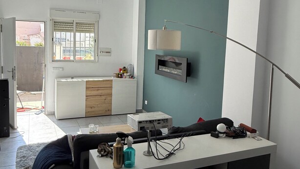 A modern living room with a sofa, a coffee table, a TV, and a kitchen area in the background.