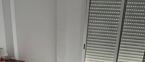 Ein Schlafzimmer mit einem Bett, einem Schreibtisch und einem Fenster mit Jalousien.