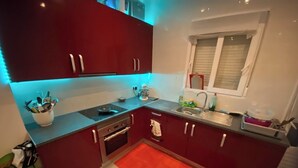 A compact kitchen with red cabinets, a window, a sink, and a red rug.