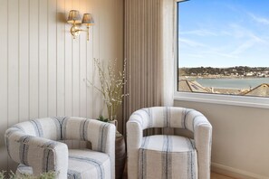 A room with two striped armchairs, a wall-mounted lamp, a vase with white flowers, and a view of a coastal area through a window. - New for 2026  Rosemerryn , Holiday Home Padstow with breathtaking estuary views (Padstow)