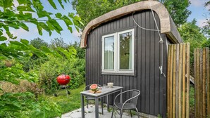 A small wooden structure with a window, a table with chairs, and a red barbecue grill in the background. - 1 bedroom gorgeous home in Gilleleje (Gilleleje)